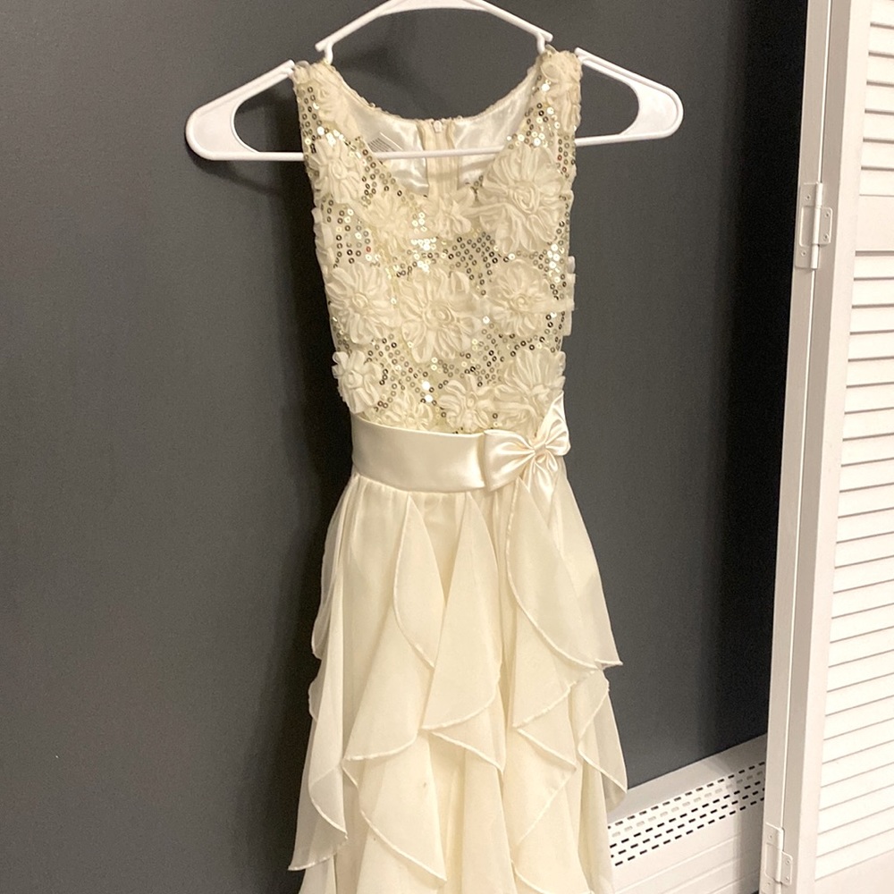 A sequined off white dress is with flower and ribbon detail